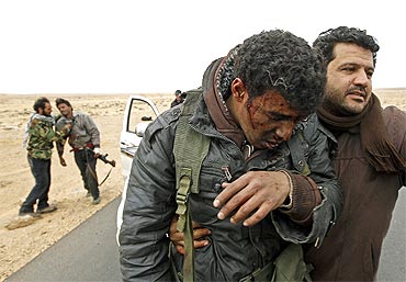 Injured rebels are helped out of a car during a battle along the road between Ras Lanuf and Bin Jiwad
