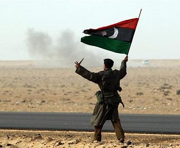 A rebel fighter holds a Kingdom of Libya flag and a knife during shelling by soldiers loyal to Libyan leader Muammar Gaddafi in a battle near Ras Lanuf