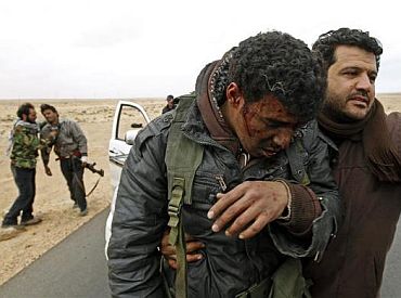 Injured rebels are helped out of a car during a battle along the road between Ras Lanuf and Bin Jiwad