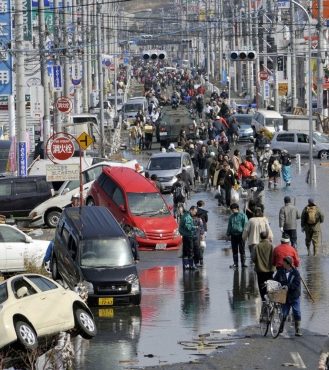 People walk along a flooded street in Ishimaki City, Miyagi Prefecture