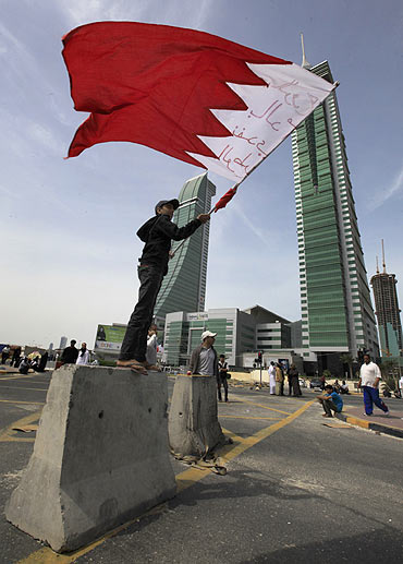 An anti-government protester waves the Bahraini flag as he stands on a roadblock used to prevent riot police from entering the junction of Bahrain Financial Harbour in Manama
