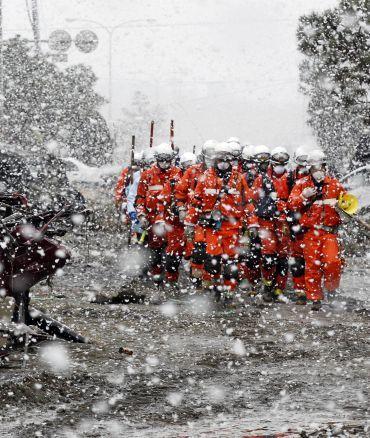 Heavy snow falls on rubble and rescue workers at a devastated factory area hit by an earthquake and tsunami in Sendai