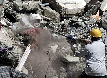 A rescue worker sprays a body with a special disinfection powder after it was discovered in the debris of a building in Bhuj