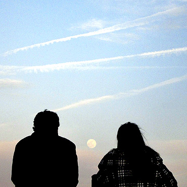 The moon rises over the skyline of New York as people stand along Hudson River in Hoboken, New Jersey