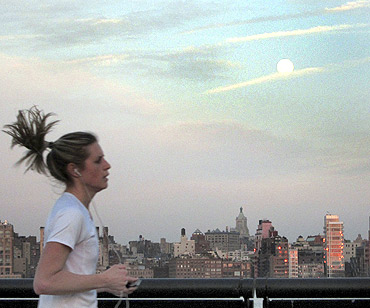 The moon rises over the skyline of New York as a jogger runs along Hudson River in Hoboken, New Jersey