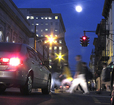 The moon rises as people cross a street in Hoboken, New Jersey