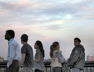 The moon rises over the skyline of New York as people stand along the Hudson River in Hoboken, New Jersey
