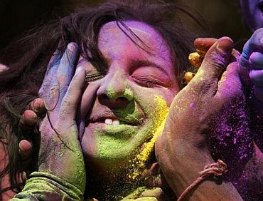 People apply coloured powder to a woman's face as they celebrate Holi