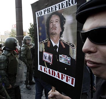 A demonstrator holds a poster with the picture of Libya's leader Muammar Gaddafi is front of riot policemen during a protest against the visit by US President Barack Obama, in Santiago