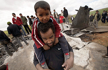 A man carries his son as they stand at a destroyed US Air Force F-15E fighter jet after it crashed