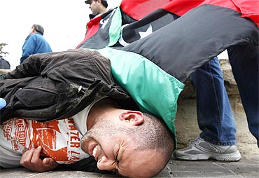 An injured anti-Gaddafi protester lies on the ground after clashes with the police