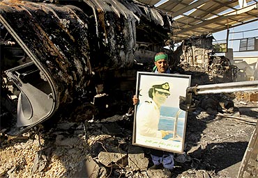 A Libyan holds a poster of Muammar Gaddafi at a naval military facility damaged by air strikes