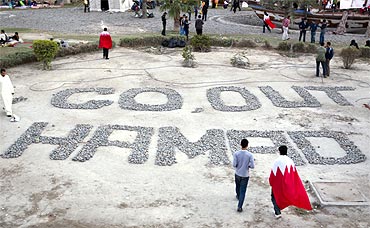 Anti government demonstrators walk around a message written with stones and addressed to King Hamad