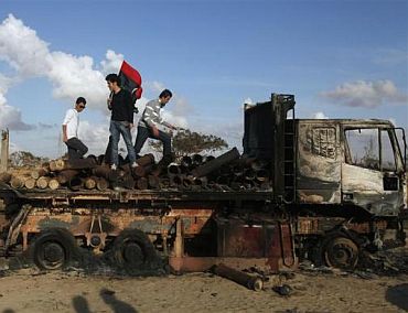 People stand atop a destroyed truck loaded with weapons belonging to forces loyal to Libyan leader Muammar Gaddafi