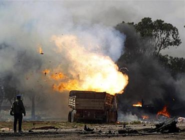 A rebel fighter looks at burning vehicles belonging to forces loyal to Libyan leader Muammar Gaddafi after an air strike by coalition forces