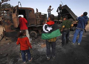 People look at weapons belonging to forces loyal to Libyan leader Muammar Gaddafi, destroyed by a coalition air strike, along a road between Benghazi and Ajdabiyah