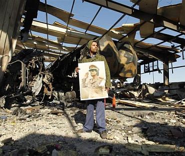 A Libyan holds a poster of Libya's leader Muammar Gaddafi at a naval military facility damaged by coalition air strikes last night in eastern Tripoli