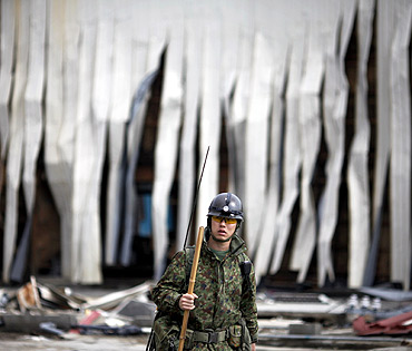 A member of Japan Self Defense Force walks in front of a destroyed building at the port of Kesennuma