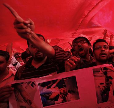 Protesters shout slogans while standing underneath Bahrain's national flag during a protest against Bahrain's King Hamad bin Isa Al-Khalifa