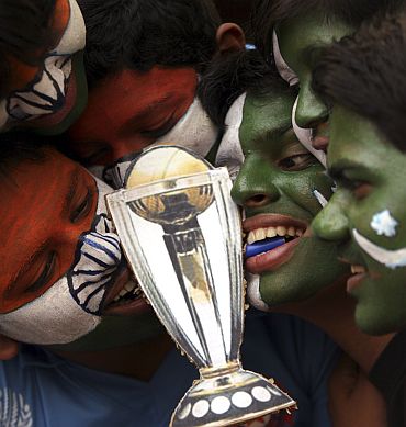 Cricket fans with their faces painted with the Indian and Pakistani national flags pose as they play tug-of-war for a replica of the Cricket World Cup trophy with their teeth, in Hyderabad