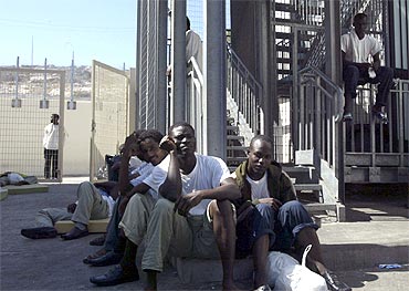 Migrants sit inside the main gate of a holding centre in Italy