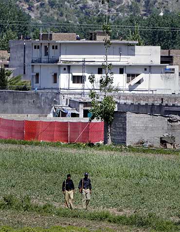 Pakistani policemen walk past Osama's compound, surrounded in red fabric