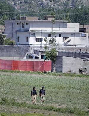 Pakistani policemen walk past a compound, surrounded in red fabric, where locals reported a firefight took place overnight