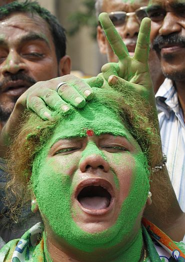 A supporter with her face smeared in green powder, a colour of the Trinamool Congress party, shouts slogans as others show the victory sign on a street in Kolkata
