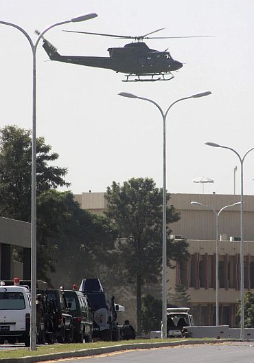A military helicopter flies overhead as security forces surround a white van used by gunmen during an attack on the Pakistan army headquarters in Rawalpindi