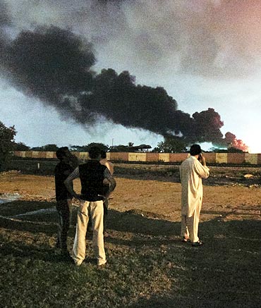 Men watch as a plume of smoke rises from the Mehran naval aviation base after it was attacked by militants in Karachi