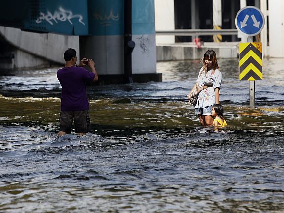 A resident uses his mobile phone to take a picture of his family at a flooded street in Bangkok