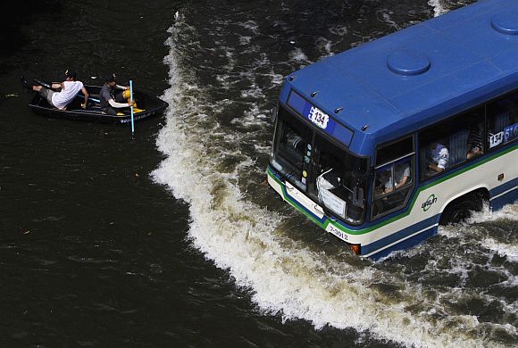 Residents travel on a boat as a bus drives on a flooded street in Bangkok