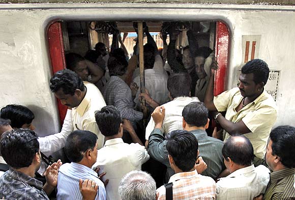 Commuters try to get in through an open doorway of a suburban train during the morning rush hour in Mumbai