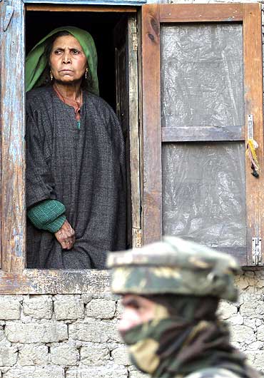 A Kashmiri woman looks out from the window of her house as an army soldier keeps guard