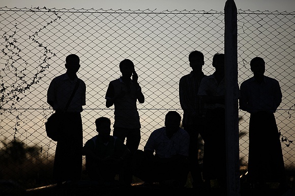 People watch from behind a fence of the airport as Clinton is welcomed upon her arrival to Myanmar's capital Naypyitaw