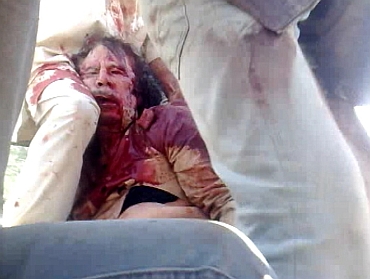 Former Libyan leader Muammar Gaddafi, covered in blood, is surrounded on a truck by NTC fighters in Sirte