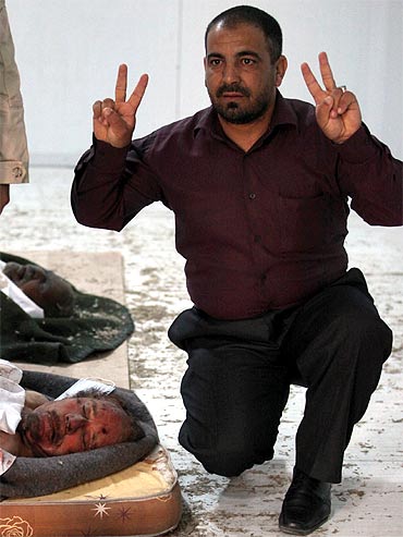 A resident flashes the victory sign near the body of slain Libyan leader Muammar Gaddafi at a storage freezer in Misrata