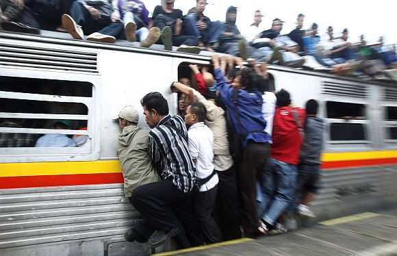 People hang onto an entrance of a commuter train which will transport them to Jakarta, in Depok, Indonesia's West Java province