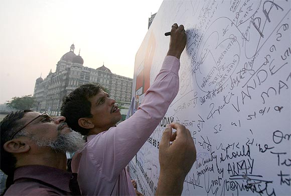 People sign and write messages on a banner during a protest rally against the 26/11 attacks