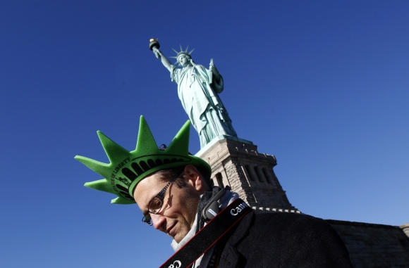 A visitor wearing a foam crown walks beneath the Statue of Liberty after ceremonies marking the 125th anniversary of the Statue at Liberty Island in New York