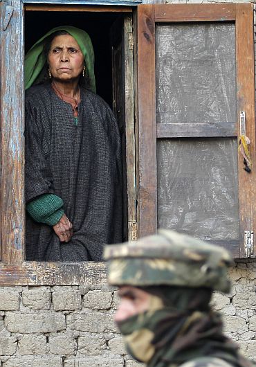 A file picture of a Kashmiri woman looking out of the window of her house as an army jawan guards during a gunbattle with militants near Srinagar