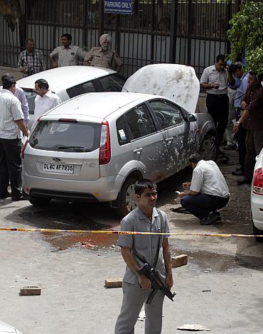A security guard keeps watch as forensic officials examine a car after a blast outside the high court in New Delhi