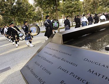 A line of bagpipers walk towards the stage past the North Pool at the National September 11 Memorial