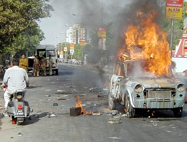 A man rides past a burning car during the 2002 riots in Ahmedabad