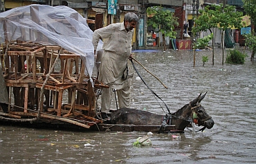 A man rides his donkey cart loaded with chairs through a flooded street, after a heavy downpour in Lahore