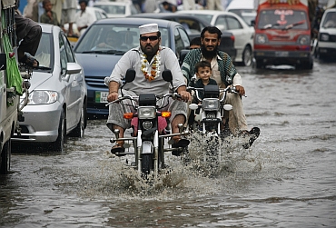 Residents ride motorcycles through a flooded street after heavy rains in Peshawar