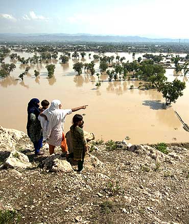 A family points towards partially submerged houses while taking refuge on a hilltop overlooking the flooded town of Nowshera, northwest Pakistan.