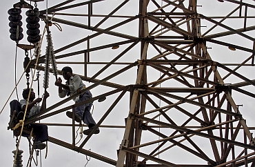 Employees of Gujarat Energy Transmission Corporation Limited work on a high transmission electric pylon on the outskirts of Ahmedabad