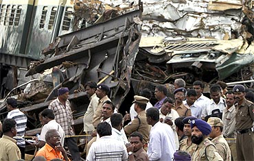 Railway officials and police stand in front of the damaged coaches of a passenger train