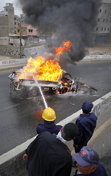 Firefighters extinguish a burning vehicle which was set ablaze by MQM protesters in Karachi